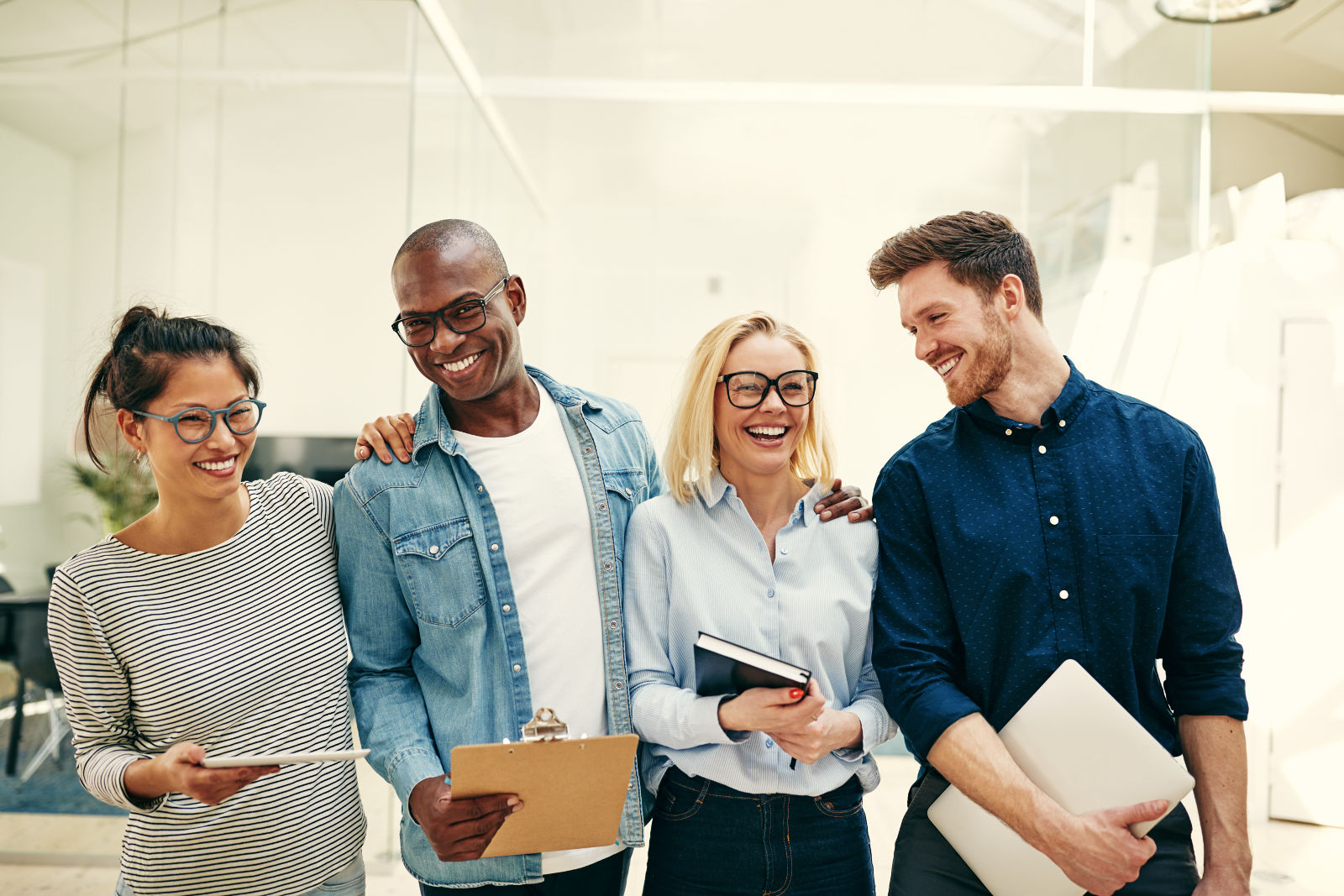 A diverse group of businesspeople laughing together in an office, representing the positive impact of workplace wellbeing initiatives.