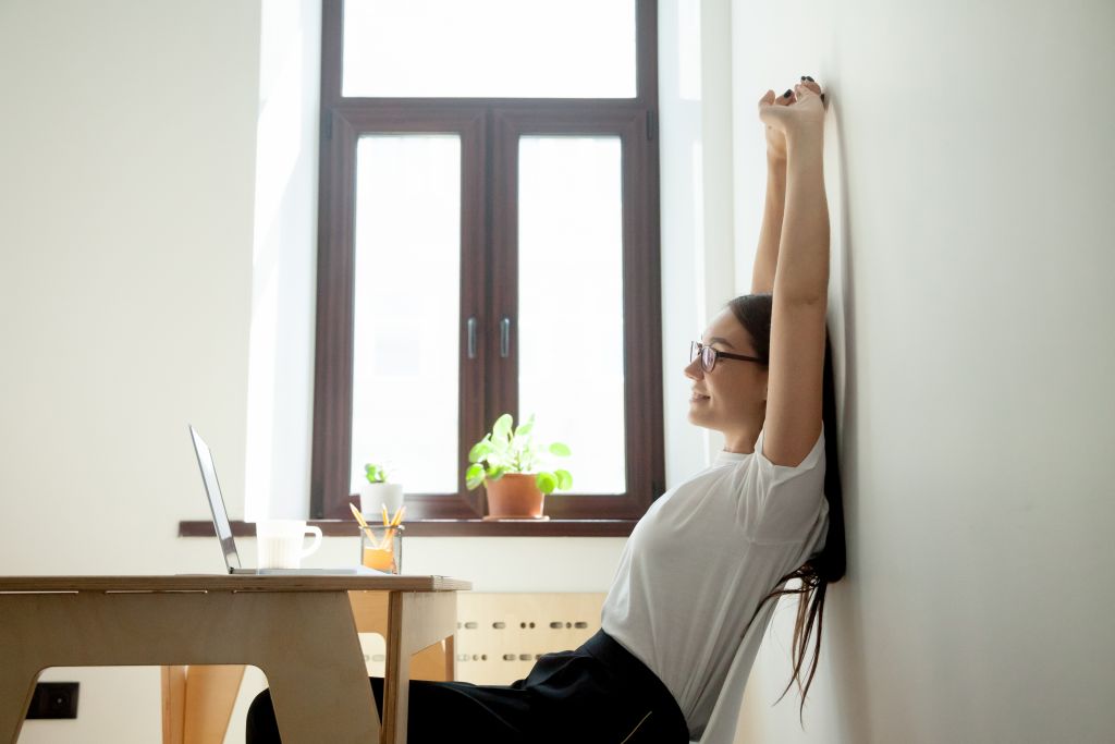 Businesswoman stretching at her desk in a bright, modern office, taking a mindful break to support work-life balance and wellbeing.Businesswoman stretching at her desk in a bright, modern office, taking a mindful break to support work-life balance and wellbeing.