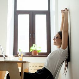 Businesswoman stretching at her desk in a bright, modern office, taking a mindful break to support work-life balance and wellbeing.Businesswoman stretching at her desk in a bright, modern office, taking a mindful break to support work-life balance and wellbeing.