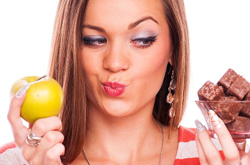 Young woman choosing an chocolate between an apple and a chocolate - isolated on white