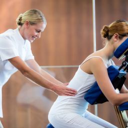Woman receiving a seated chair massage in a workplace setting, looking relaxed and supported by a professional therapist.