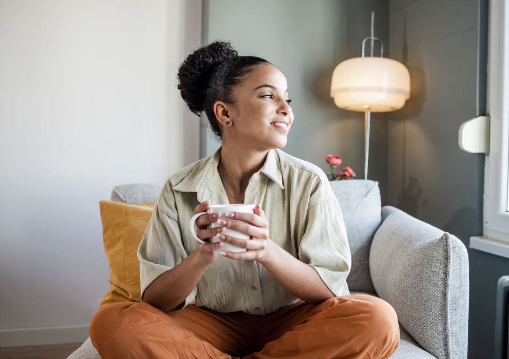young woman relaxing on comfortable chair with hot drink looking cosy
