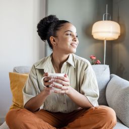 young woman relaxing on comfortable chair with hot drink looking cosy