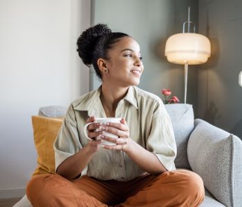 young woman relaxing on comfortable chair with hot drink looking cosy