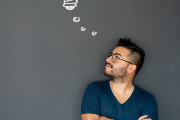 Young-man-standing-in-front-of-a-dark-background-with-an-illustration-of-a-lightbulb-representing-thinking