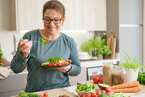 A woman in a kitchen surrounded by plant based food eating a from a colourful plate