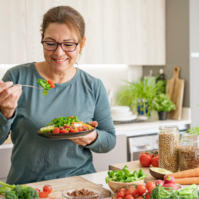 A woman in a kitchen surrounded by plant based food eating a from a colourful plate