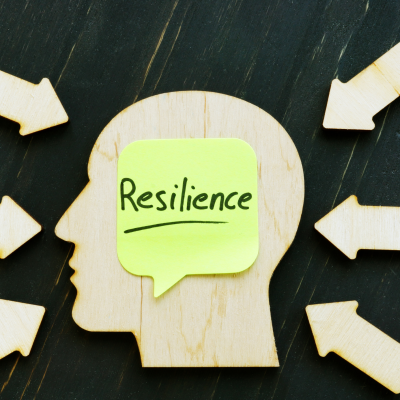 An image of a flat wooden head with a post it and the word resilience on it